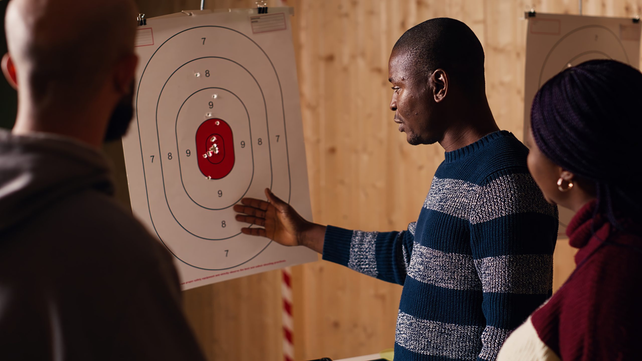 Shooting range safety officer explaining bullseye scoring system to group of mates. African american firing range expert teaching bullseye points system and discussing industry regulations